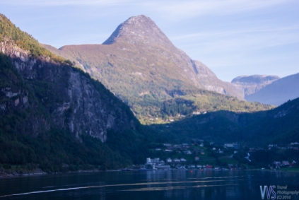 The view of Geiranger village with a mighty Åkerneset in the background. The mountain is slightly eroding and is expected some day to crash down into a fjord, which will create a tsunami - an event that already happened a few times in Norwegian fjords.